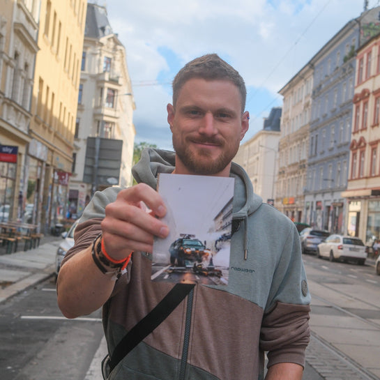 elbracho Postkarte 'Räumpanzer' wird auf einer bunten Straße in Leipzig-Connewitz in die Kamera gehalten